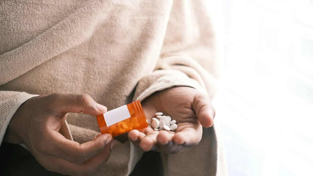 Person pouring white pills from a prescription bottle into a hand
