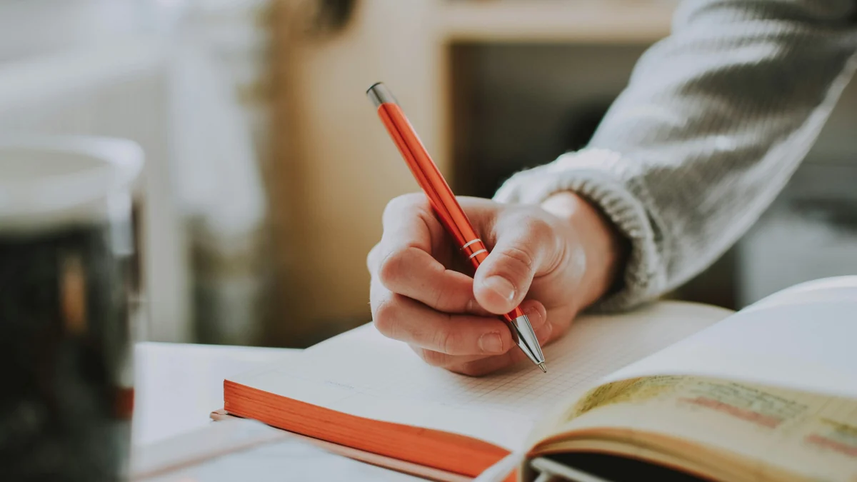 Hand writing notes in a notebook with an orange pen